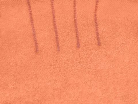 Textile. Detail view of four mauve-pink lines stitched into a coral-pink blanket.