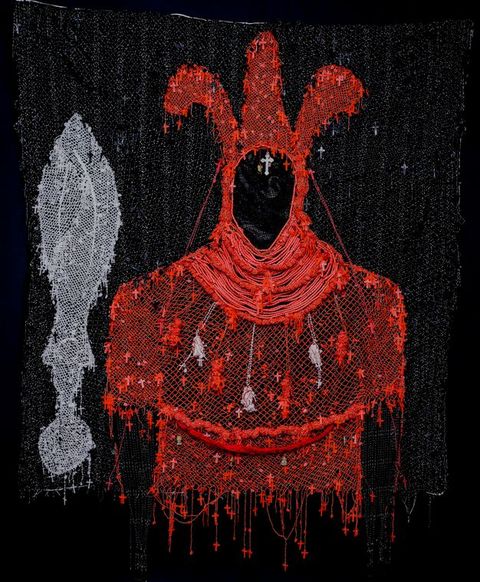 Mixed media. A red silhouette of a costume seems drawn in thread against a black background. The hood has three tall lobes. Tiny red crosses and a few sculptures hang all over the costume. A silvery grey object with a blade-like form above a circle is to the left.